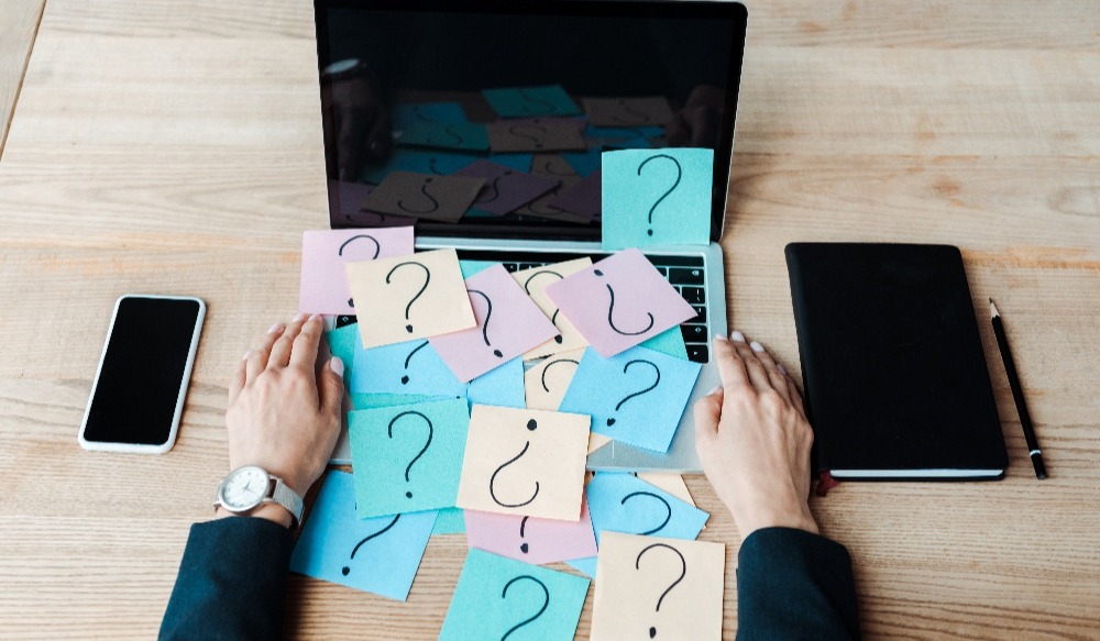 Computer covered in sticky notes that have question marks on them